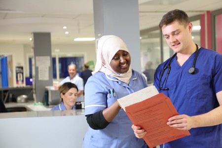 Doctor and HCA are stood looking in a patients notes infront of the gynaecology ward nurses desk