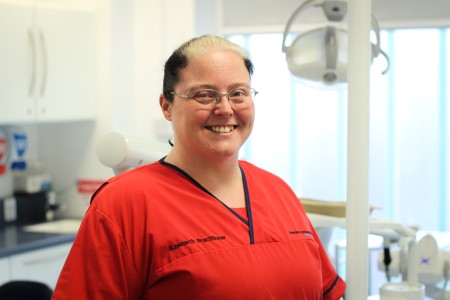Image of nurse standing in a theatre, wearing a red uniform.