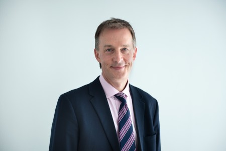 A photo of new Chief Medical Officer Andy Nicolson standing against a plain background wearing a suit and tie